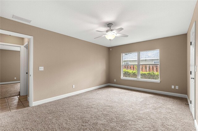 carpeted empty room with baseboards, a ceiling fan, visible vents, and tile patterned flooring