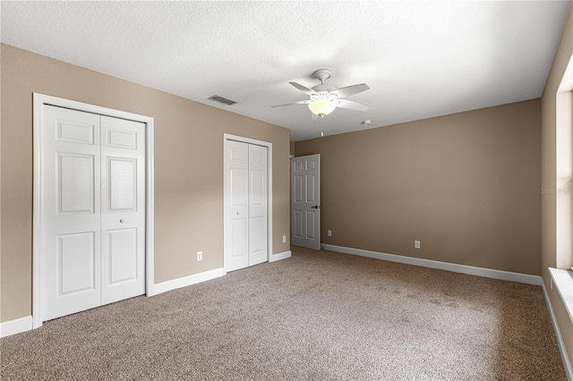unfurnished bedroom featuring a textured ceiling, visible vents, carpet flooring, multiple closets, and baseboards