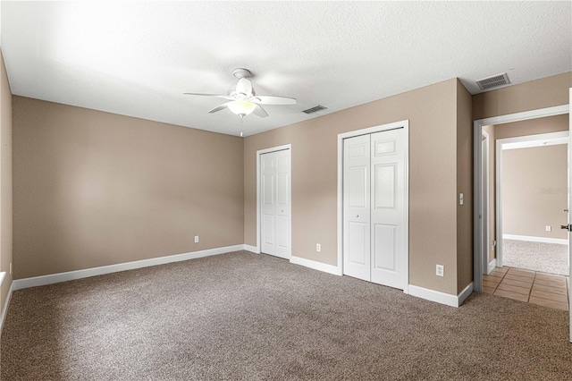 unfurnished bedroom with ceiling fan, carpet floors, two closets, and a textured ceiling