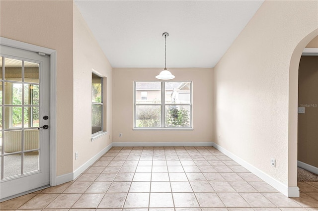 unfurnished dining area featuring baseboards, a textured wall, light tile patterned floors, lofted ceiling, and arched walkways