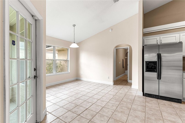 unfurnished dining area with baseboards, arched walkways, light tile patterned flooring, and vaulted ceiling