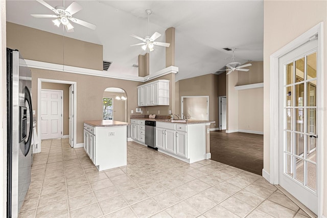 kitchen with ceiling fan, arched walkways, white cabinetry, a sink, and stainless steel fridge