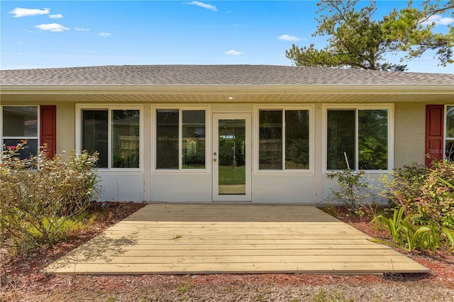 property entrance featuring roof with shingles, a wooden deck, and stucco siding