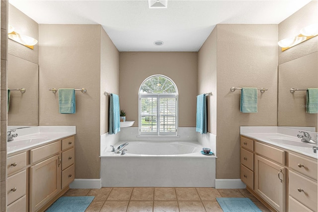 full bath featuring tile patterned floors, a bath, a sink, and two vanities
