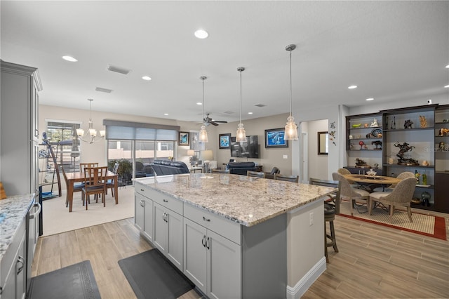 kitchen with a breakfast bar area, ceiling fan with notable chandelier, light hardwood / wood-style floors, and a kitchen island