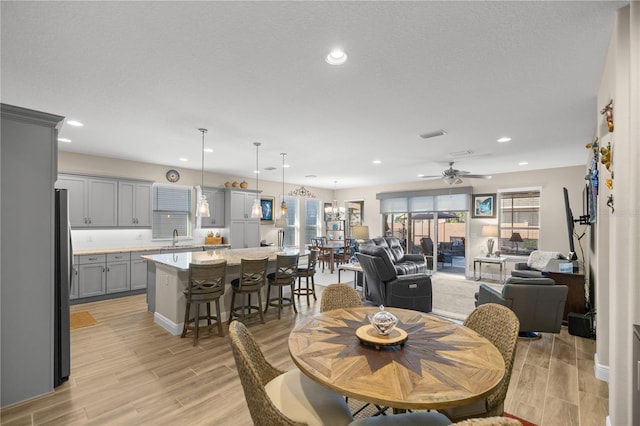 dining area featuring ceiling fan, sink, light hardwood / wood-style floors, and a textured ceiling