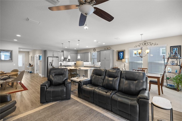 living room with ceiling fan with notable chandelier, light hardwood / wood-style floors, and a wealth of natural light