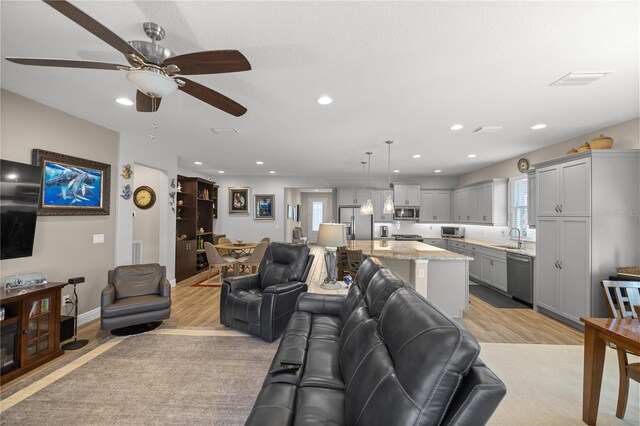 living room with ceiling fan, light wood-type flooring, and sink