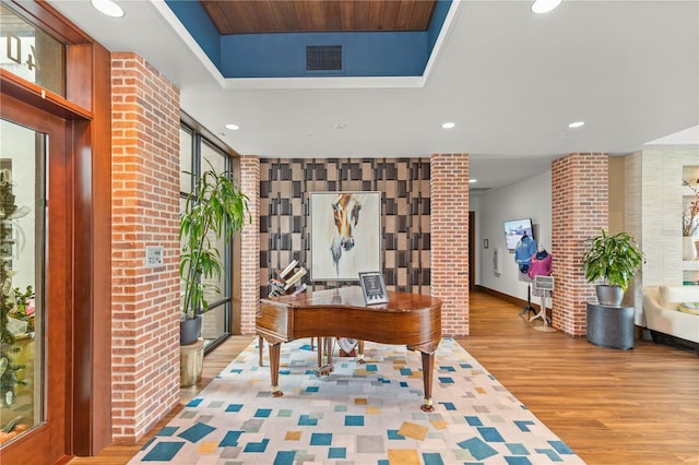 home office with light wood-type flooring, brick wall, and a raised ceiling