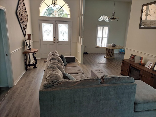 living room with a high ceiling, an inviting chandelier, light hardwood / wood-style flooring, and french doors