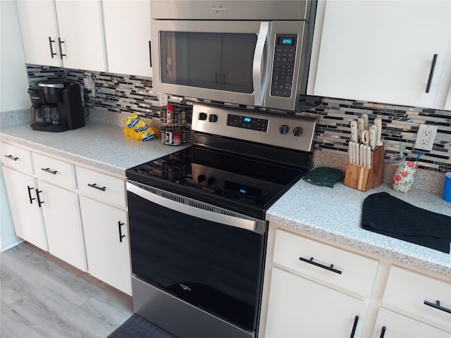 kitchen featuring stainless steel appliances, white cabinetry, light wood-type flooring, and backsplash