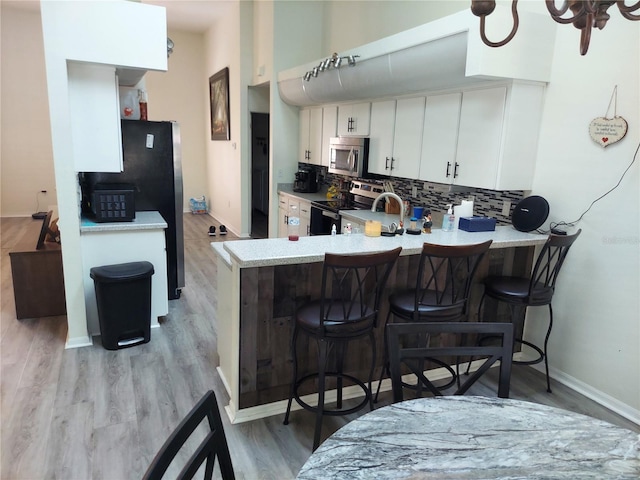 kitchen with white cabinets, kitchen peninsula, light hardwood / wood-style flooring, backsplash, and appliances with stainless steel finishes