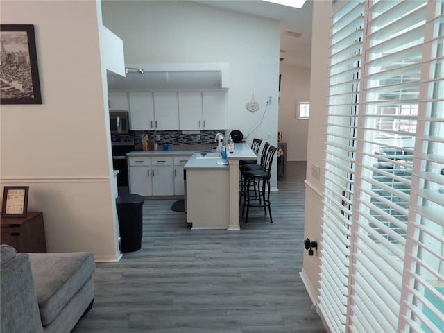 kitchen with sink, kitchen peninsula, a kitchen bar, white cabinetry, and dark hardwood / wood-style flooring