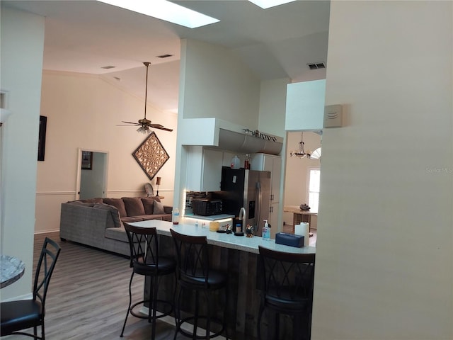 kitchen with a kitchen breakfast bar, stainless steel fridge, kitchen peninsula, dark hardwood / wood-style flooring, and lofted ceiling with skylight