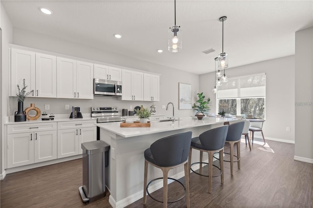 kitchen featuring white cabinetry, a center island with sink, appliances with stainless steel finishes, and decorative light fixtures