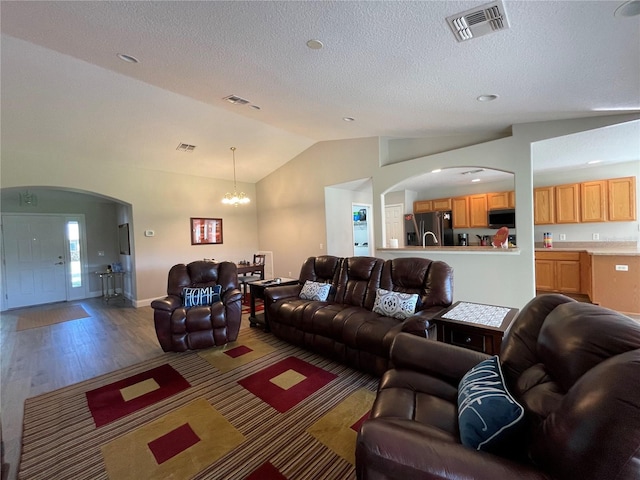 living room featuring an inviting chandelier, hardwood / wood-style floors, vaulted ceiling, and a textured ceiling