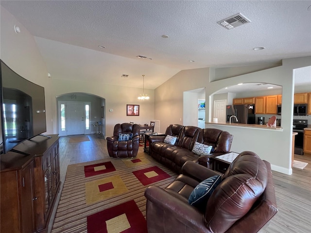 living room featuring a textured ceiling, lofted ceiling, a chandelier, and light wood-type flooring