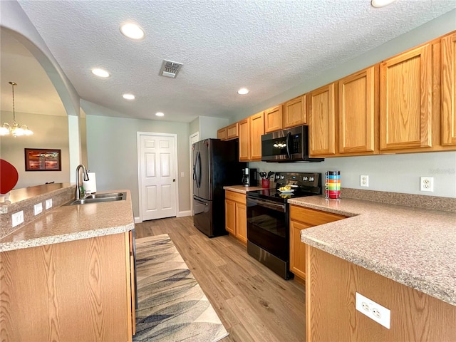 kitchen featuring light wood-type flooring, light stone counters, black appliances, sink, and pendant lighting