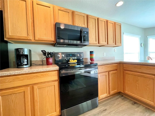 kitchen featuring appliances with stainless steel finishes, light wood-type flooring, and a textured ceiling