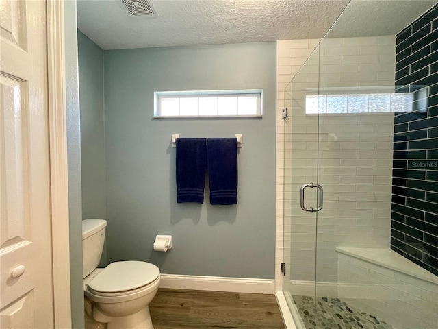 bathroom with hardwood / wood-style floors, a shower with shower door, a textured ceiling, and toilet