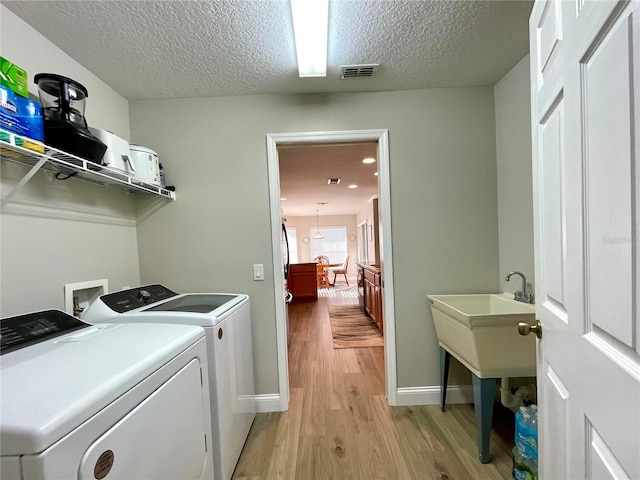 clothes washing area with washer and clothes dryer, a textured ceiling, and light hardwood / wood-style floors