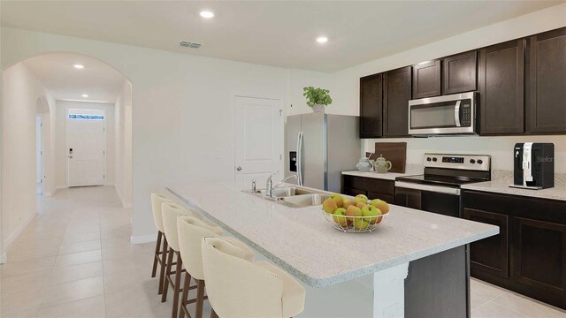 kitchen featuring appliances with stainless steel finishes, an island with sink, a breakfast bar area, dark brown cabinets, and sink