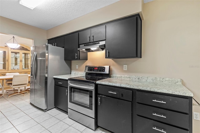 kitchen with a textured ceiling, light tile patterned floors, dark cabinets, under cabinet range hood, and stainless steel appliances