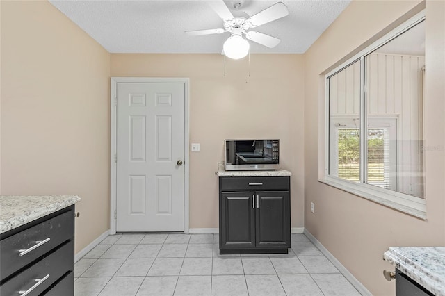 kitchen with baseboards, stainless steel microwave, light countertops, a textured ceiling, and light tile patterned flooring