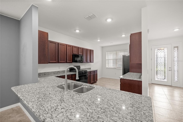 kitchen featuring kitchen peninsula, light stone countertops, sink, black appliances, and light tile patterned floors