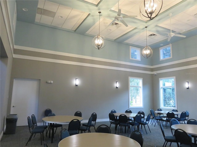 carpeted dining area with ceiling fan with notable chandelier and coffered ceiling