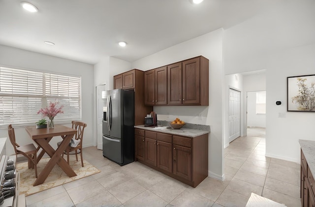 kitchen featuring dark brown cabinets, light tile patterned floors, stainless steel refrigerator with ice dispenser, and range