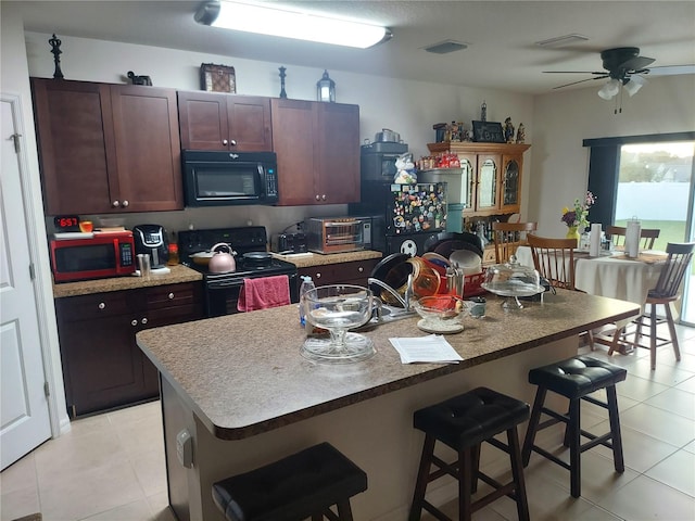 kitchen featuring black appliances, a kitchen bar, dark brown cabinets, ceiling fan, and a kitchen island with sink