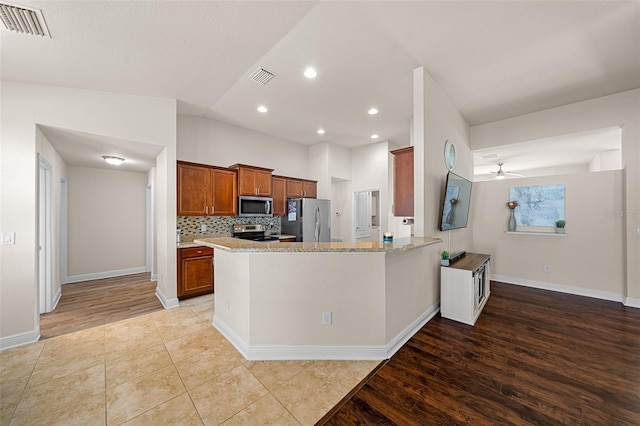 kitchen with appliances with stainless steel finishes, light stone counters, kitchen peninsula, ceiling fan, and light hardwood / wood-style flooring