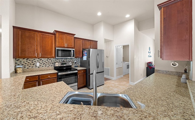 kitchen featuring light tile patterned flooring, washer and dryer, tasteful backsplash, kitchen peninsula, and appliances with stainless steel finishes