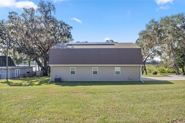 back of property with central AC, solar panels, and a yard