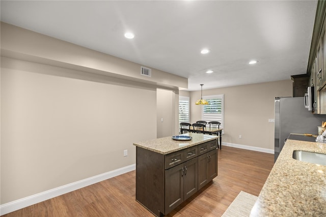 kitchen with dark brown cabinets, pendant lighting, a kitchen island, light hardwood / wood-style flooring, and light stone countertops