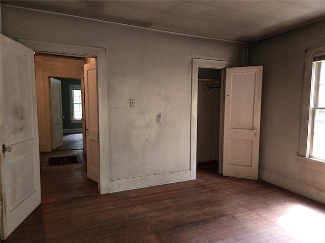 unfurnished bedroom with multiple windows, dark wood-type flooring, and a closet