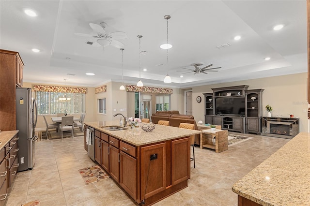 kitchen with a kitchen island with sink, stainless steel appliances, a raised ceiling, sink, and decorative light fixtures