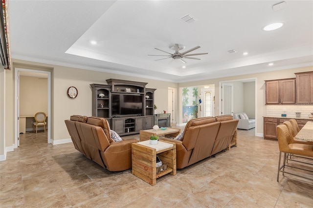 living room with ceiling fan, a tray ceiling, and ornamental molding