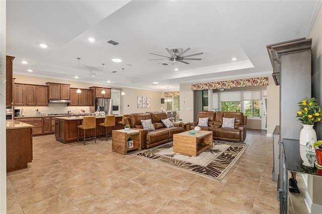 living room with ceiling fan, a tray ceiling, and crown molding