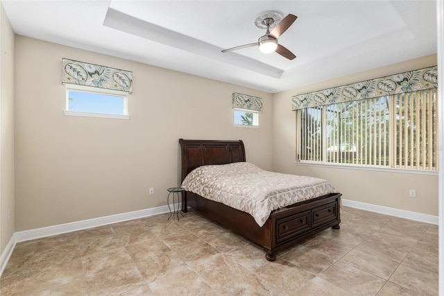 bedroom with a raised ceiling, multiple windows, and ceiling fan