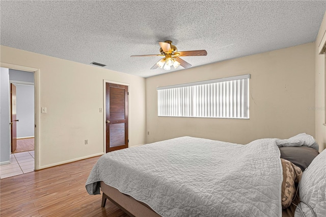 bedroom featuring a textured ceiling, a closet, light wood-type flooring, and ceiling fan