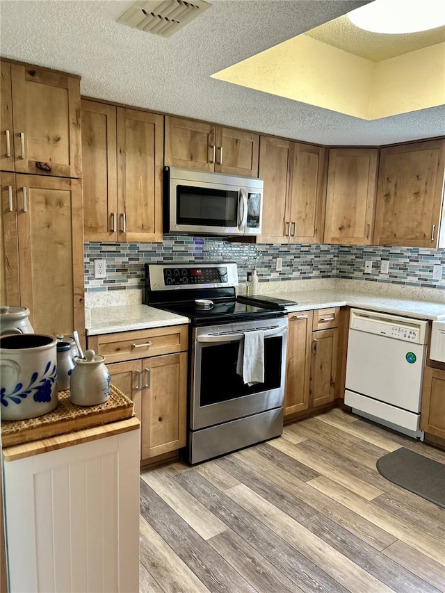 kitchen featuring brown cabinets, light wood finished floors, tasteful backsplash, visible vents, and appliances with stainless steel finishes