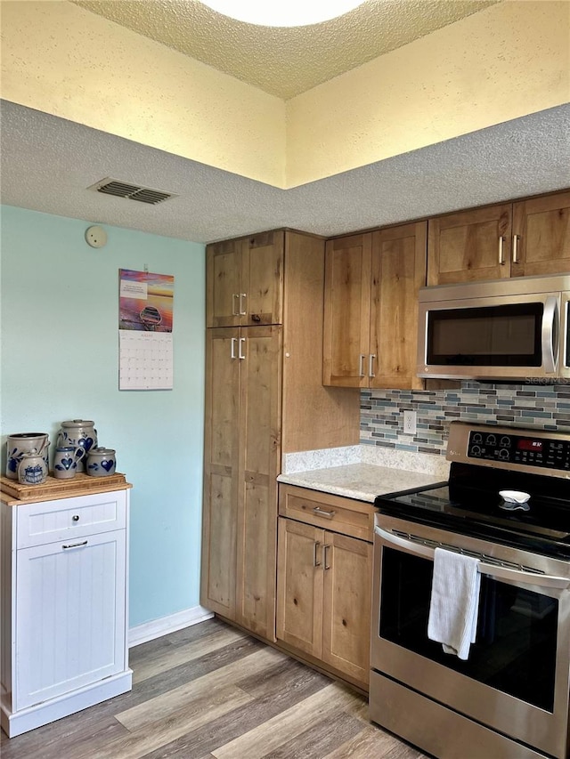 kitchen with a textured ceiling, stainless steel appliances, decorative backsplash, and light hardwood / wood-style flooring