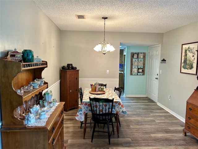 dining space featuring an inviting chandelier, a textured ceiling, and dark wood-type flooring