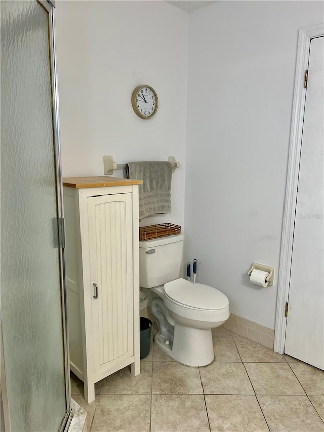 bathroom with tile patterned flooring, a shower with shower door, and toilet