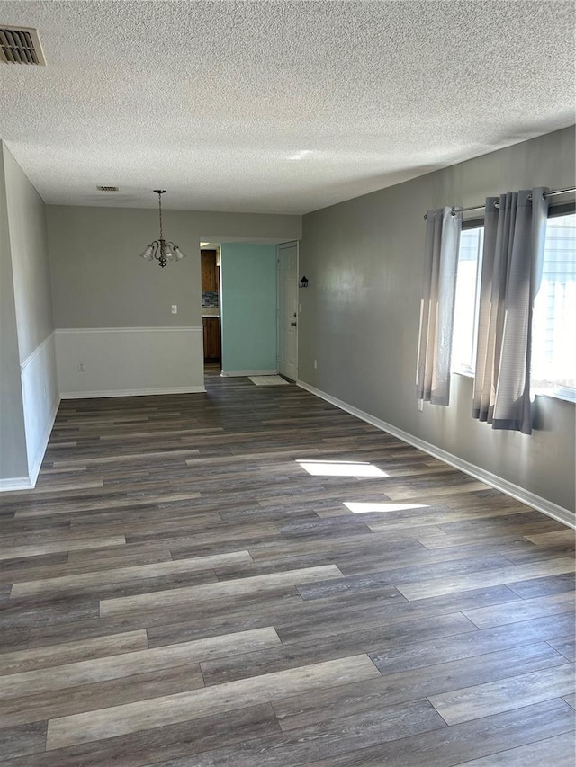 empty room featuring baseboards, a textured ceiling, visible vents, and dark wood-type flooring