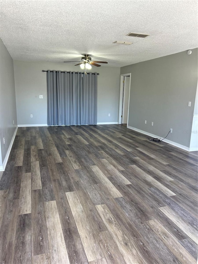 empty room with dark wood-style floors, ceiling fan, visible vents, and baseboards