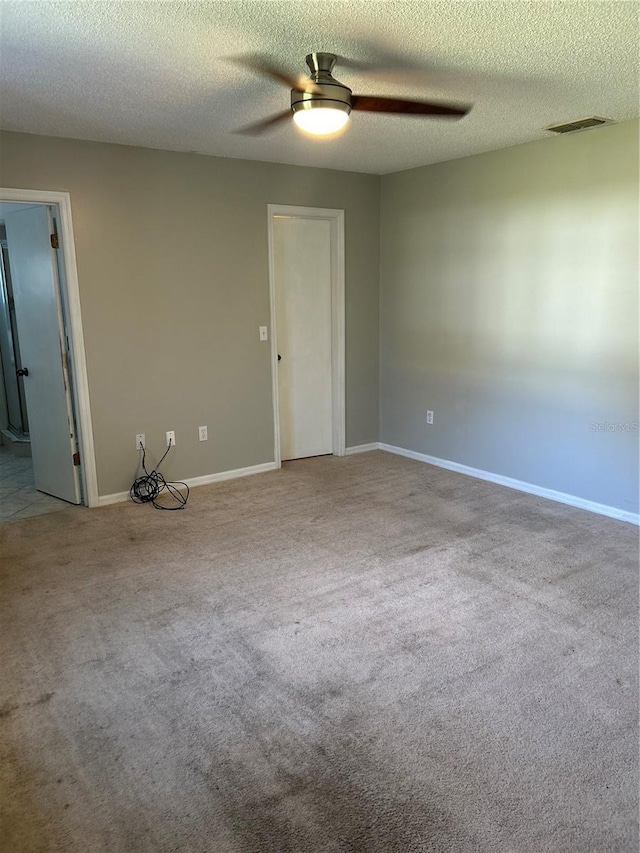 carpeted empty room featuring baseboards, a textured ceiling, visible vents, and a ceiling fan