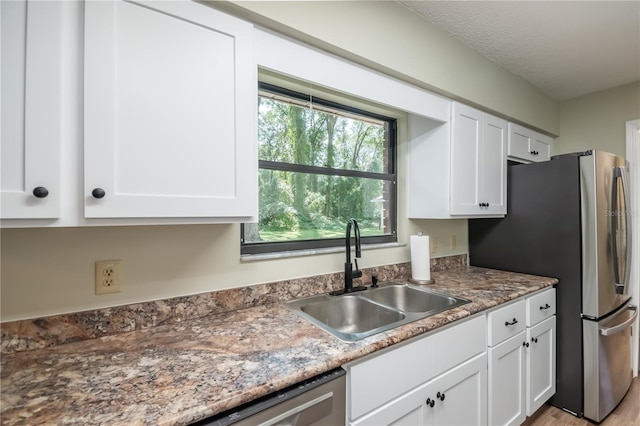 kitchen featuring light wood-type flooring, a textured ceiling, sink, white cabinets, and appliances with stainless steel finishes